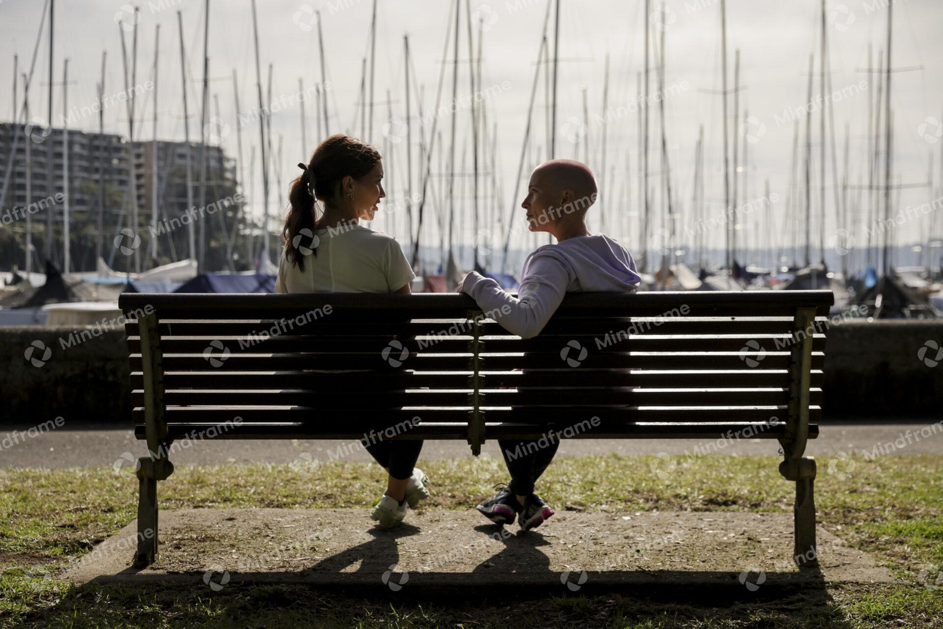 Two people talking, sitting on a bench near the water – Mindframe ...
