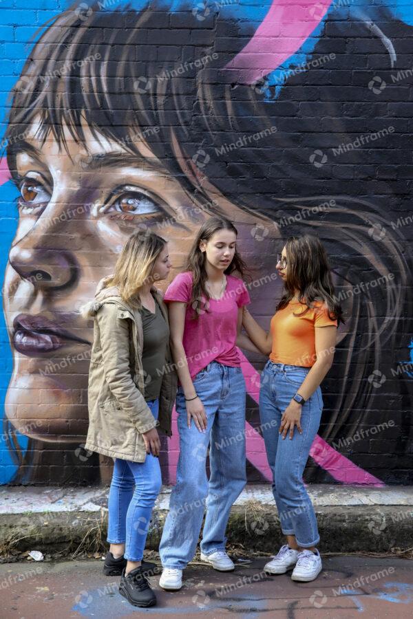 Group of young women standing outside next to mural talking