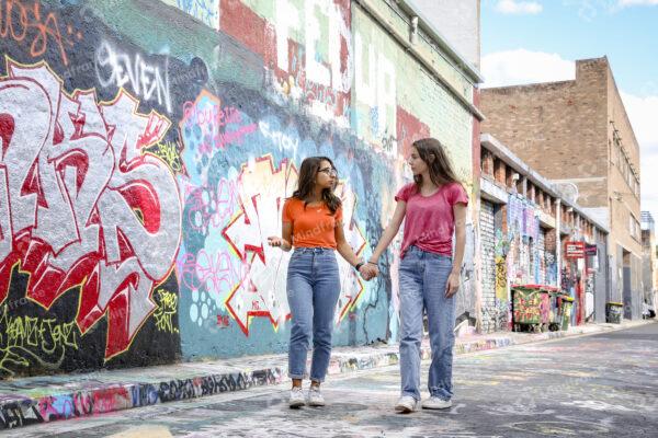 Two young women walking outside in lane talking and holding hands