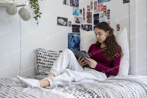 Young person using iPad sitting on bed